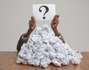 African business woman under crumpled pile of papers with hands holding a question sign